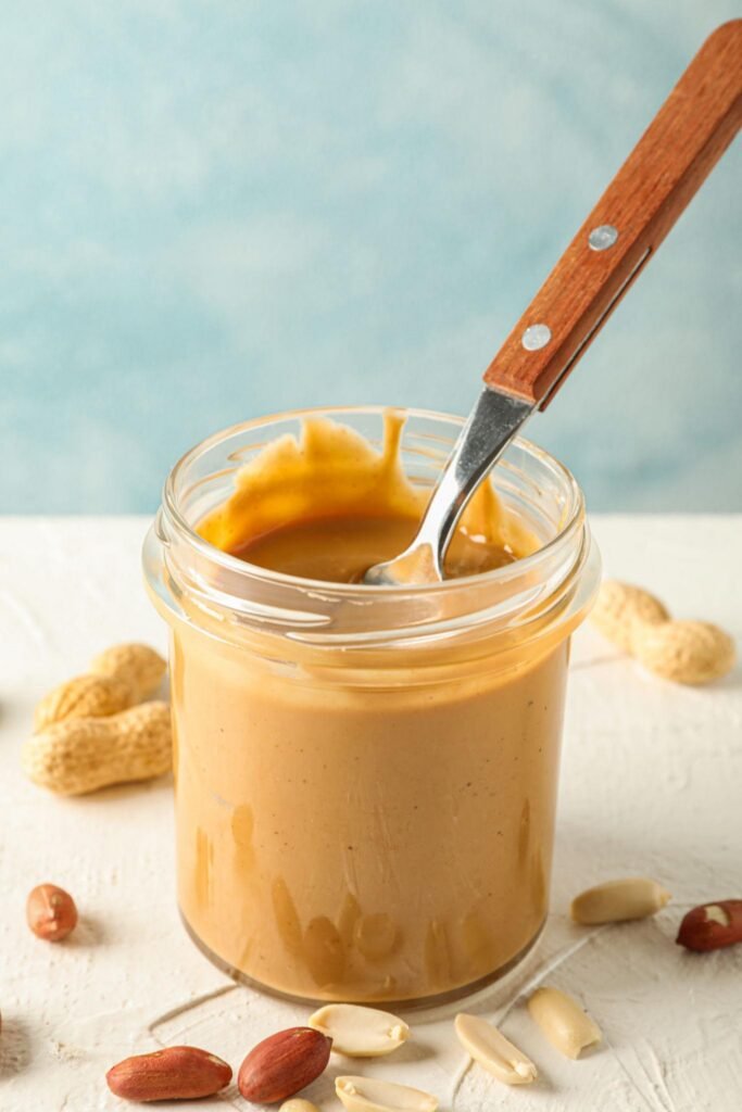 Jar of creamy peanut butter with spoon and peanuts